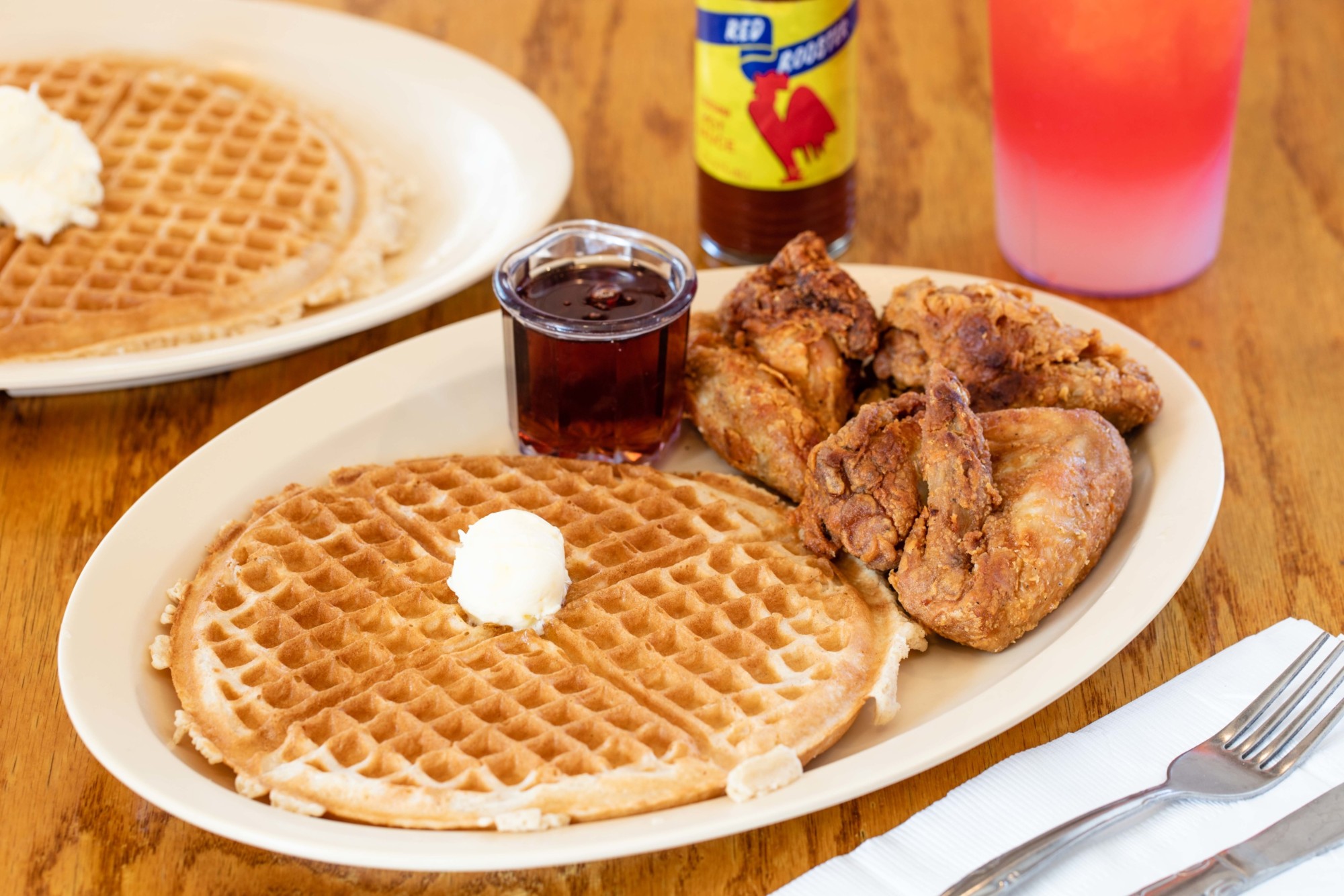 A plate of chicken and waffles with hot sauce and syrup